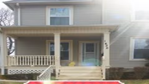 Front exterior view of a two-story house with a covered porch, beige siding, white railing, and steps leading up to the entrance. There is a window on the second floor and two windows on the first floor beside the front door.