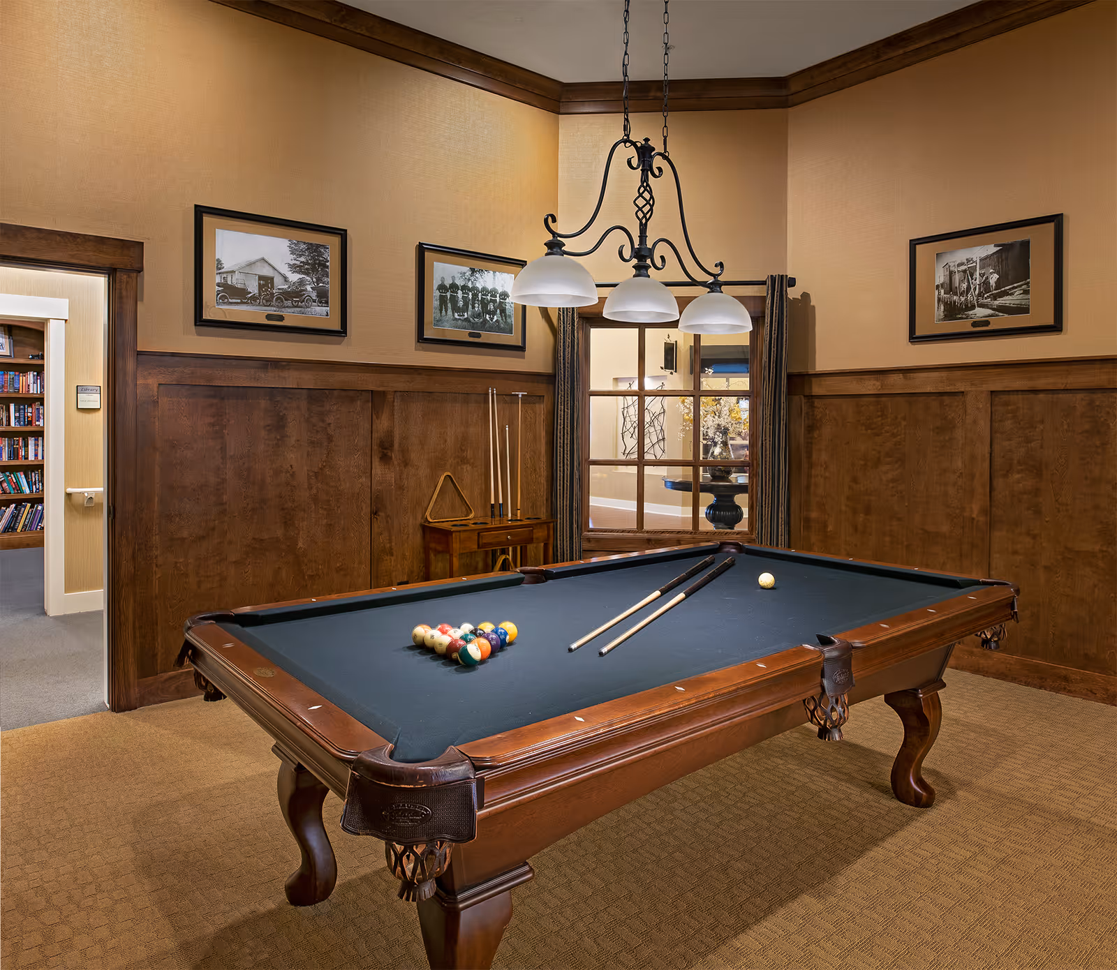 Interior room with a pool table, overhead pendant lights, wood-paneled walls and framed photographs.