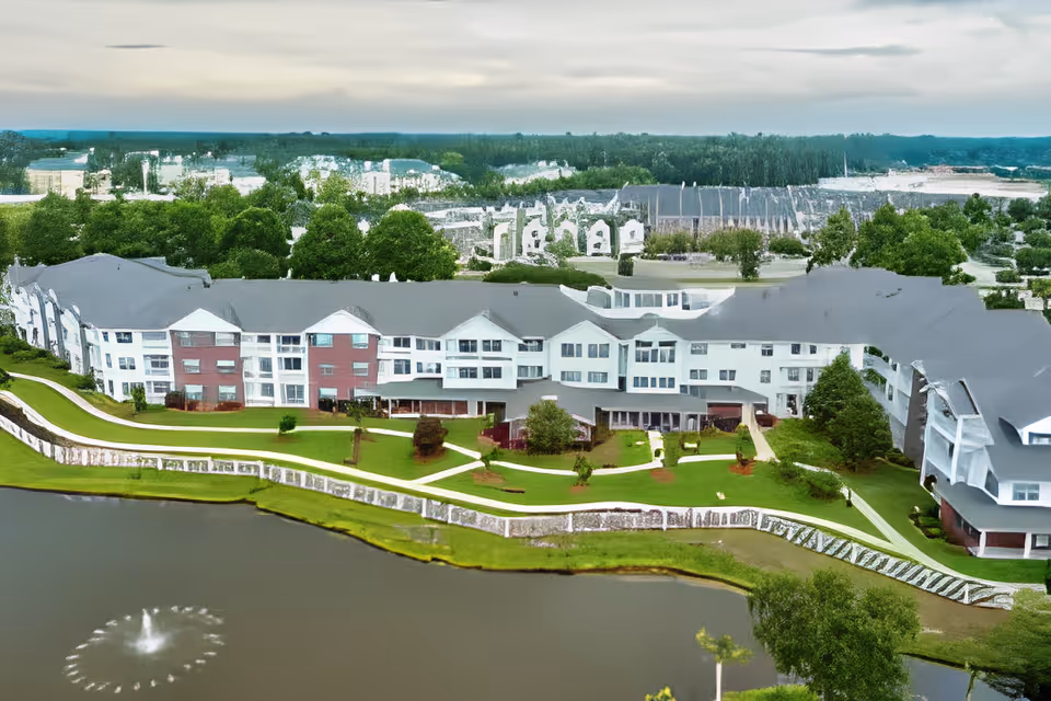 Aerial view of a multi-story senior living building with landscaped grounds and a pond with a fountain in front.