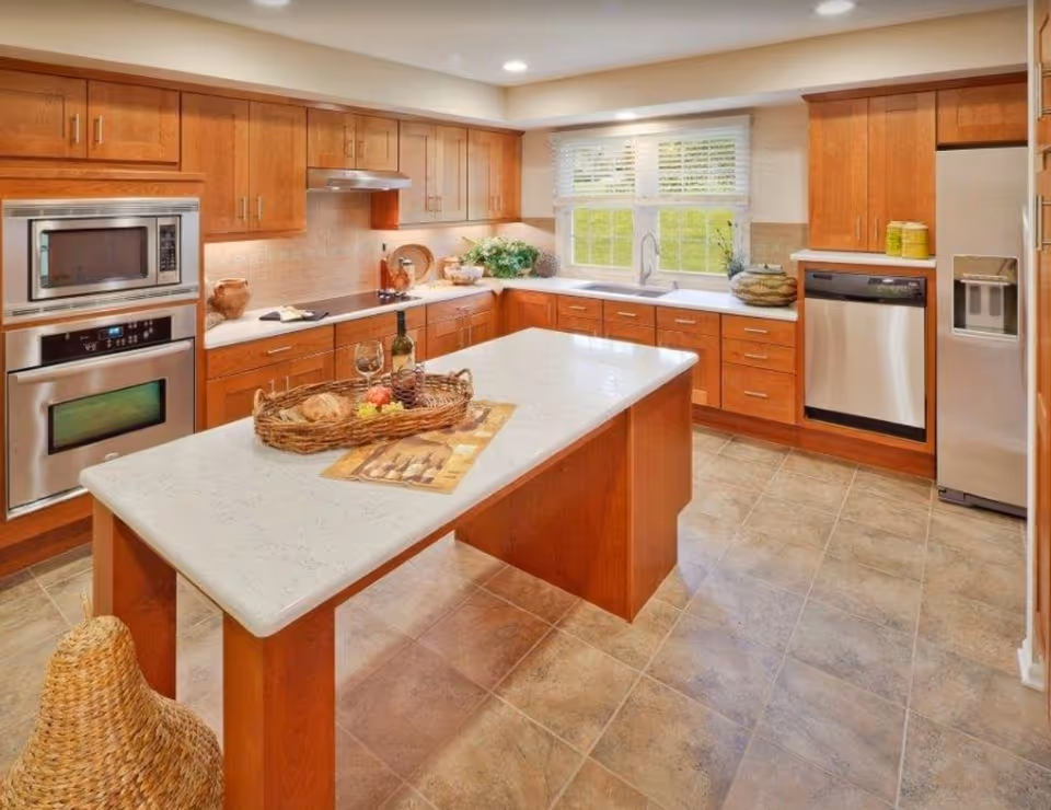 Bright modern kitchen with a central island, wooden cabinets, stainless appliances, and a window over the sink.