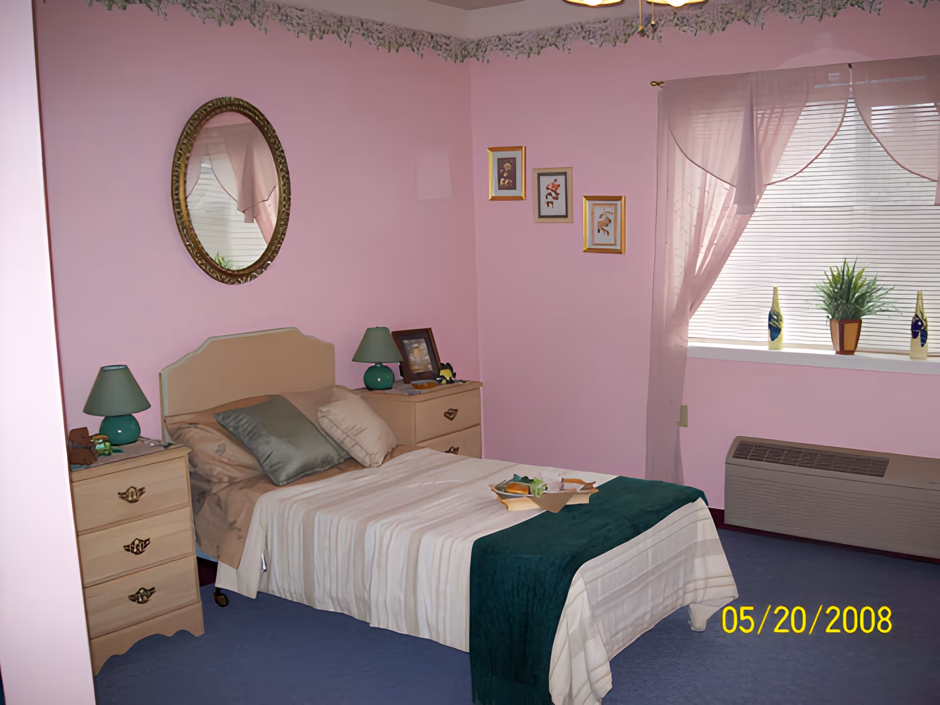 Small pink bedroom with a single bed, two nightstands with lamps, an oval mirror and a window with blinds.
