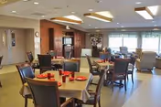Communal dining room with multiple set tables and chairs, and a lounge area with a TV and large windows.