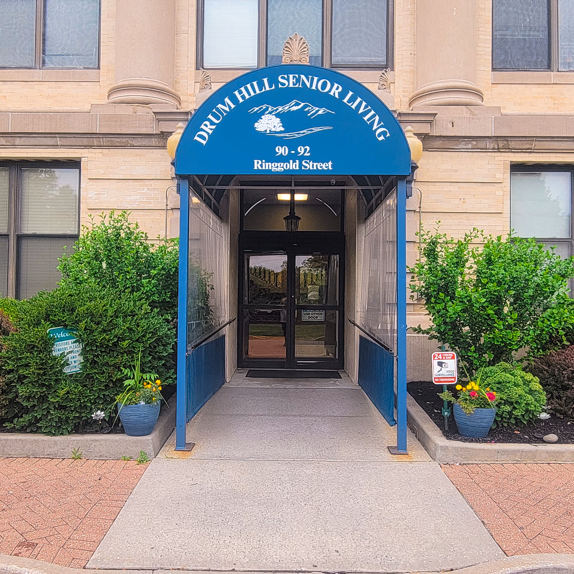 Entrance to Drum Hill Senior Living with a blue awning over the doorway showing the name and address.