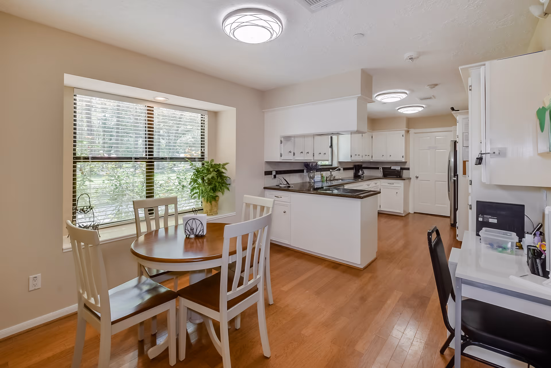 Bright open kitchen and dining area with a round wooden table by a window, white cabinetry, and a central island.