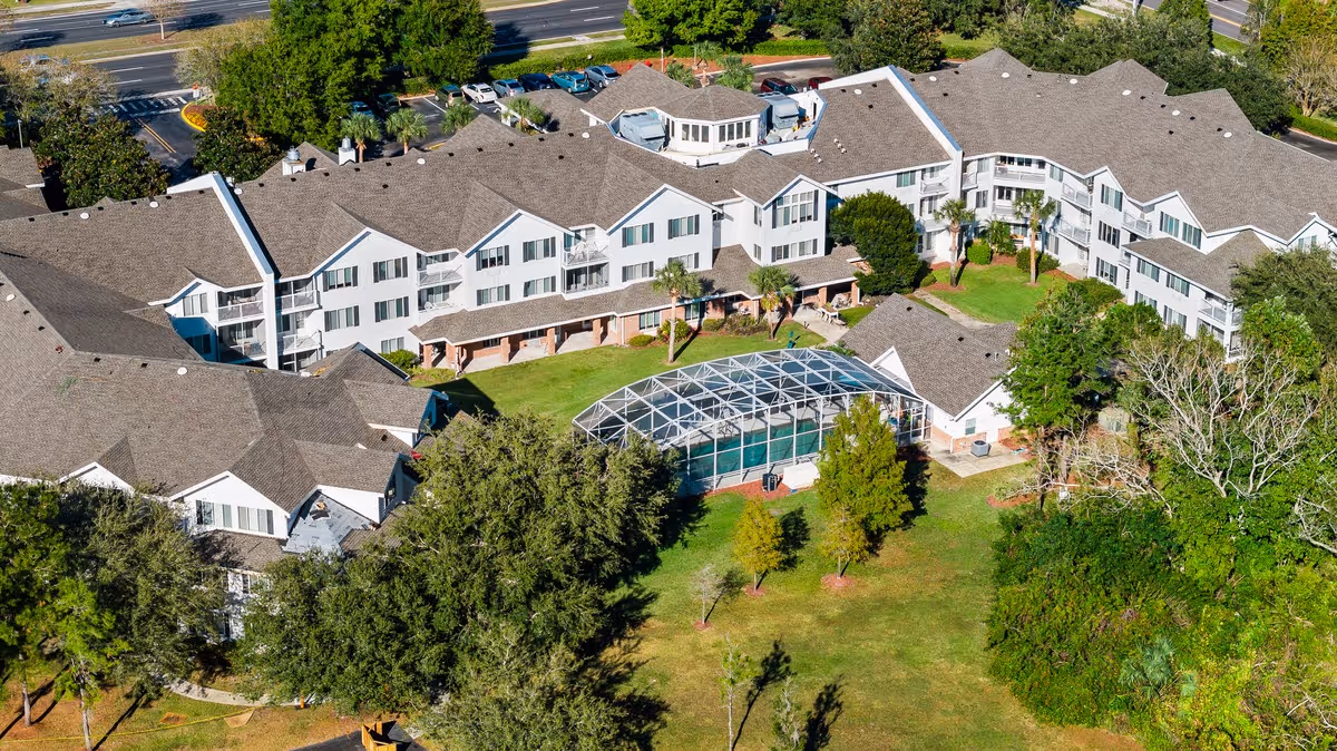 Aerial view of a multi-wing white senior living building surrounding a central lawn and a screened pool enclosure.