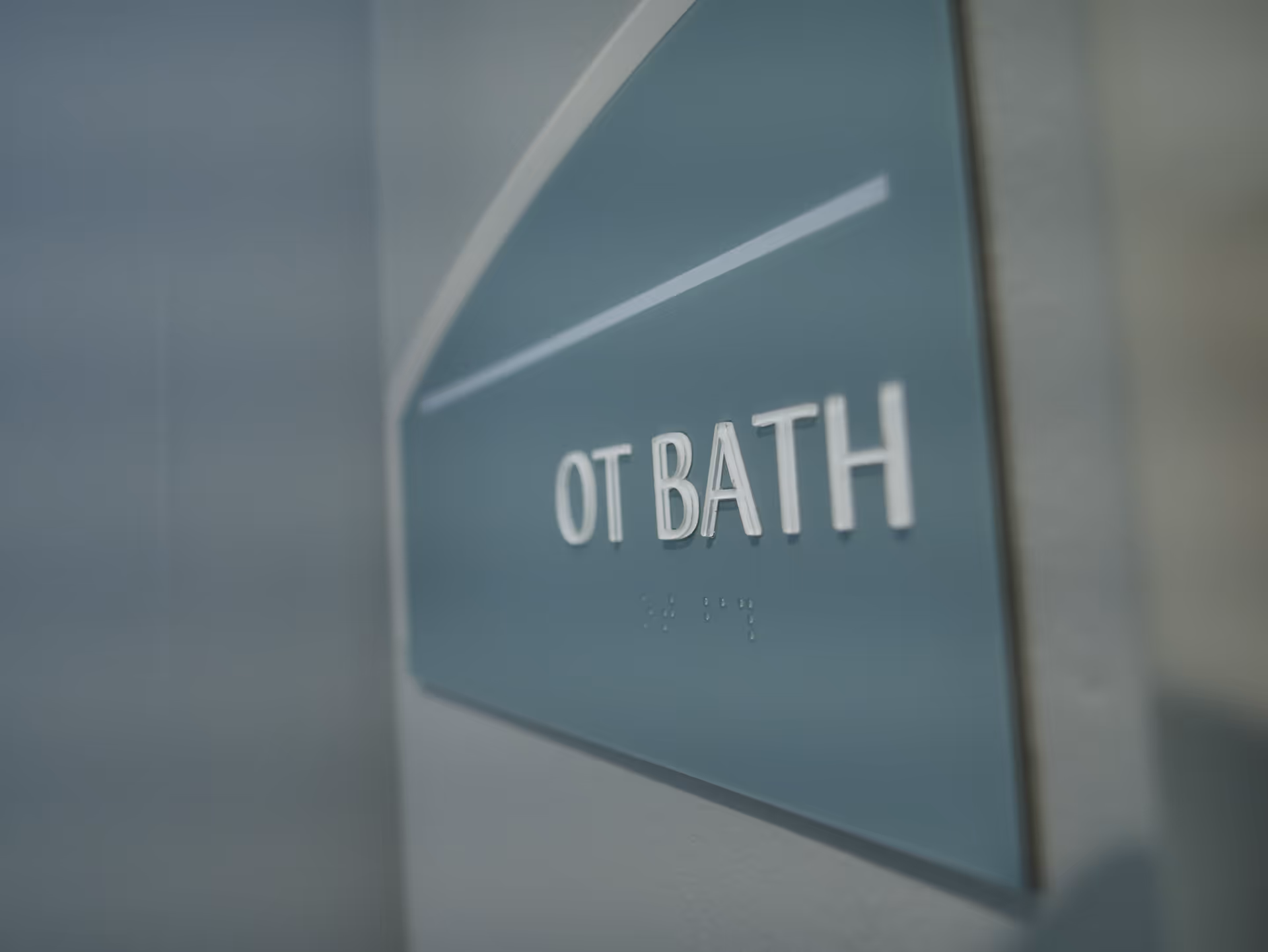Close-up of a blue and white sign on a wall that reads 'OT BATH' with Braille below the text.