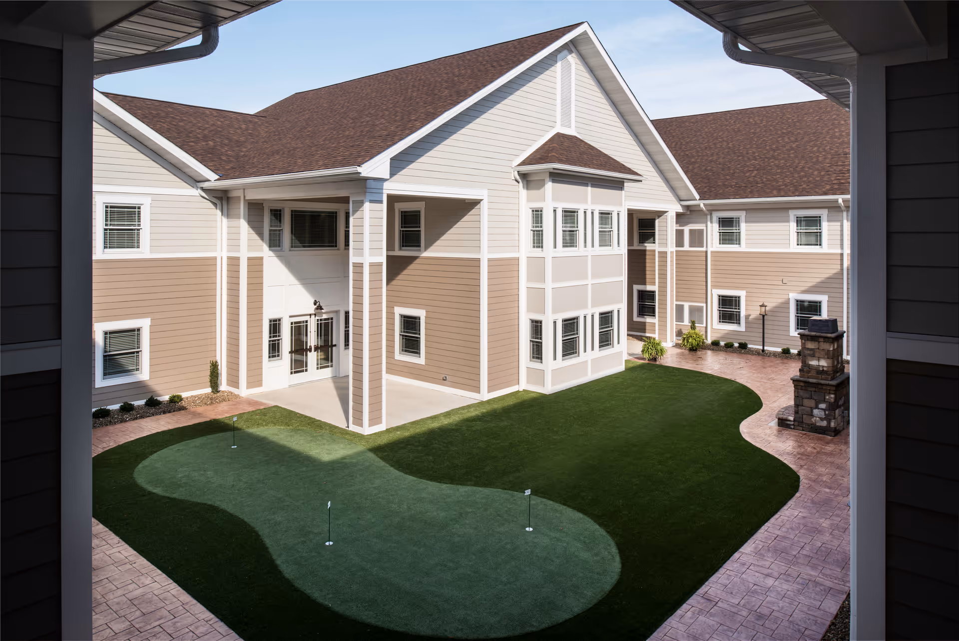 Central courtyard with an artificial putting green surrounded by a two-story beige senior living building.