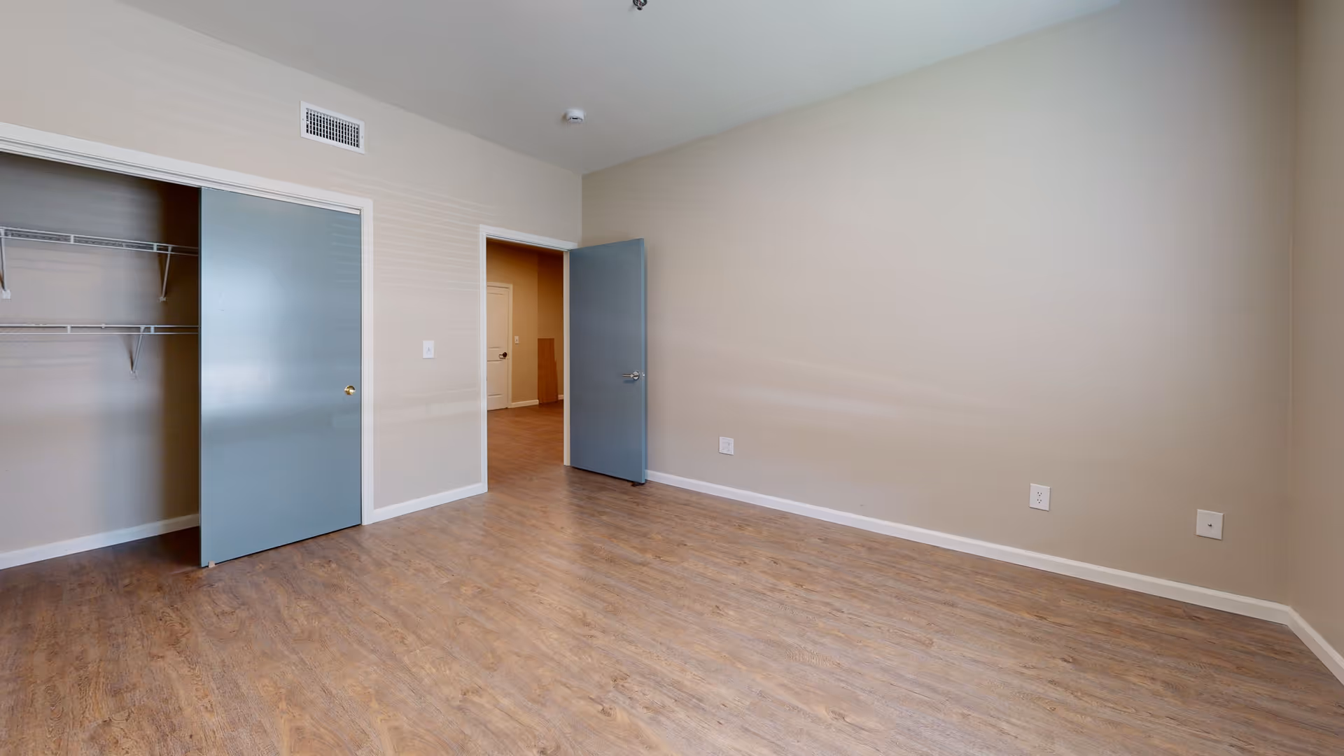 Empty room with wood flooring, beige walls, an open closet with sliding blue doors, and an open blue door leading to another room.