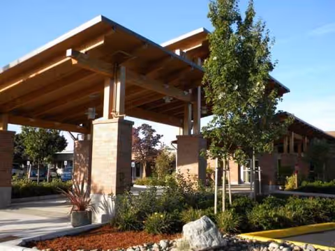 Covered entrance with wooden beams, brick columns, and landscaped front yard of a senior facility.