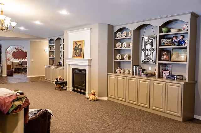 Spacious living area with a central fireplace flanked by built-in shelves and cabinets displaying decorative plates, framed pictures, and small decor items.