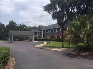 Exterior view of Plantation Oaks Senior Living Residence with brick building, driveway, and landscaping.