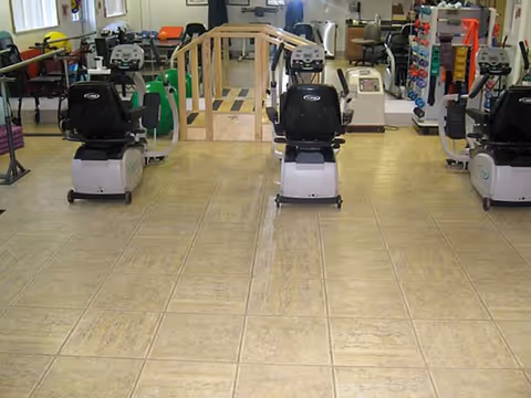 A rehabilitation gym with several recumbent exercise bikes, a small wooden practice bridge, and various therapy and fitness equipment.