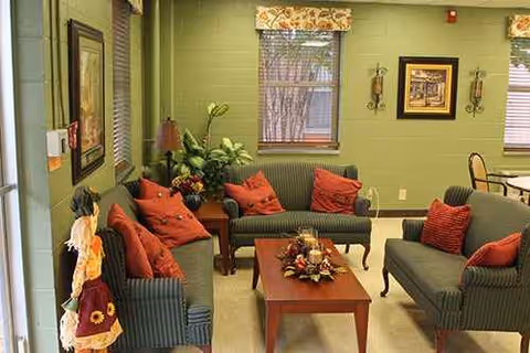 Cozy green living room lounge with red cushions, plants, and a central coffee table.