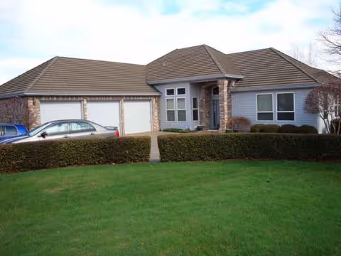 Front view of a single-story house with a two-car garage and trimmed shrubs.