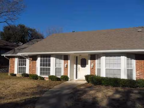 Single-story brick senior living facility exterior with front entrance and trimmed shrubs.