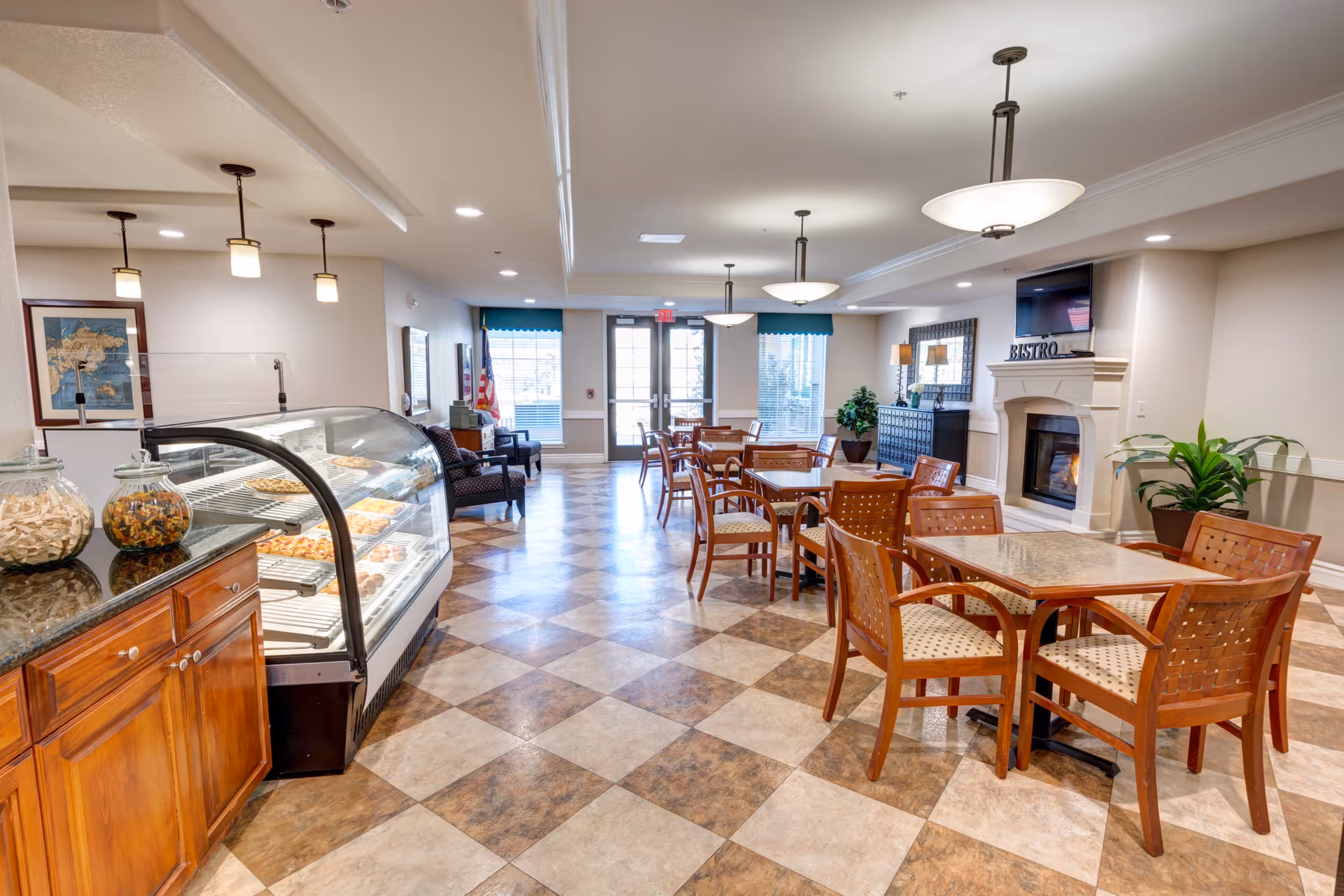 Bright senior living dining area with tables and chairs, a glass pastry display case, and a fireplace labeled "BISTRO".