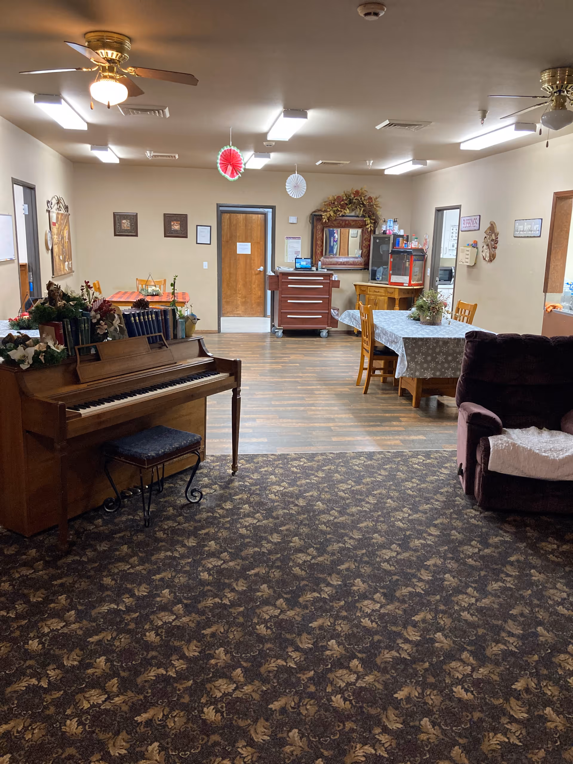 A senior living common room with a piano, dining tables, and seating.