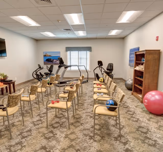 Well-lit interior fitness/activity room with rows of chairs holding small hand weights, exercise machines, and stability balls.