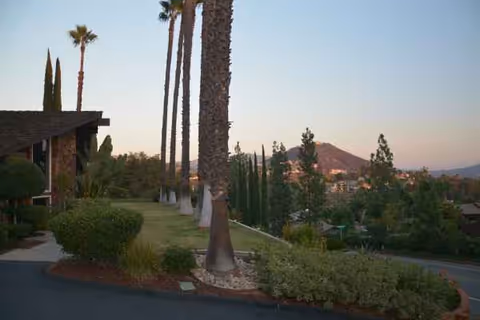 Exterior view of Villa Alegre Senior Care Homes with palm trees, shrubs, and hills.
