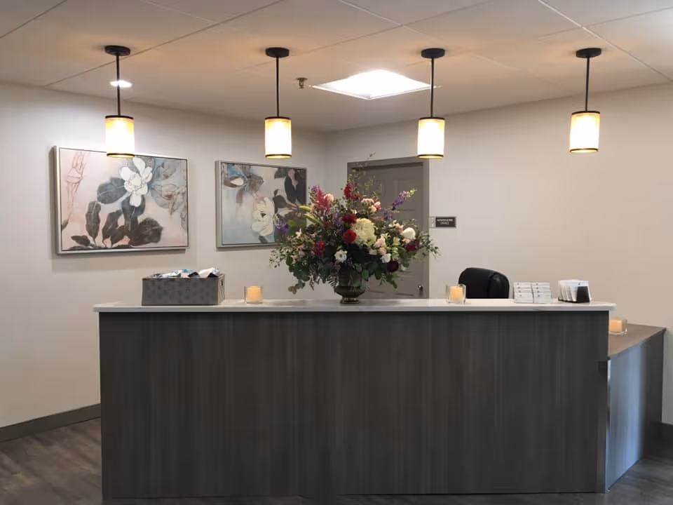 Reception desk in a clean lobby with a large floral arrangement, pendant lights, and wall art.