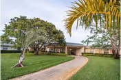 Front exterior of a single-story health and rehabilitation building with a curved driveway, manicured lawn, and palm trees.