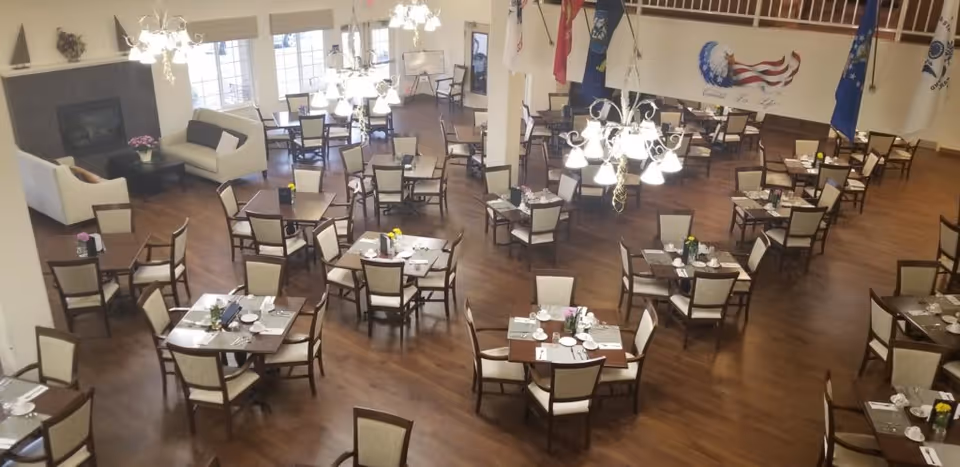 Spacious dining room with multiple set tables and chairs, chandeliers, and a seating area by a fireplace.