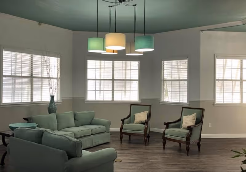 Bright common lounge with mint-green sofas and armchairs beneath a multi-shade pendant light and large windows.
