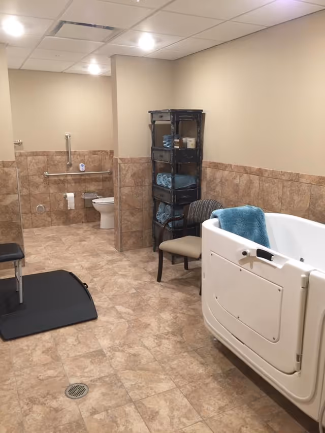 Accessible bathroom featuring a walk-in tub, a toilet with grab bars, towel shelving and seating.