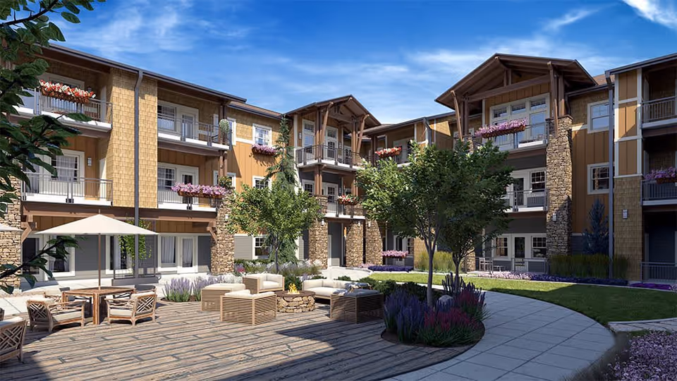 Sunny courtyard with outdoor seating, trees, planters and balconies of a three-story senior living building.