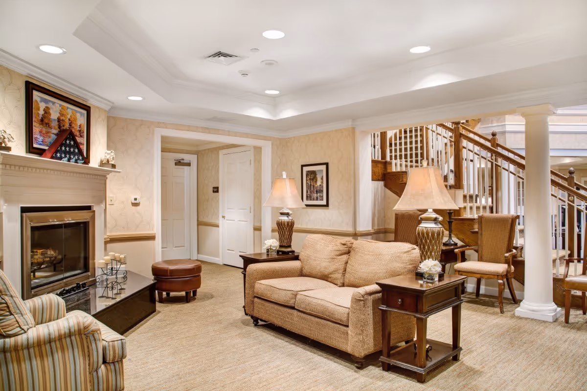 Cozy furnished living room with a sofa, armchairs, lamps, fireplace, and a staircase in the background.