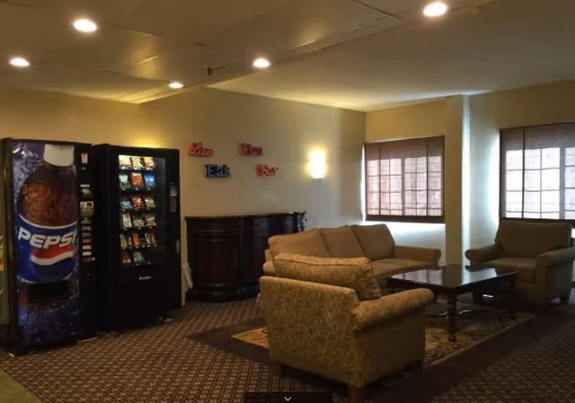 Communal lounge with sofas, armchairs, a coffee table and vending machines against a wall under ceiling lights.