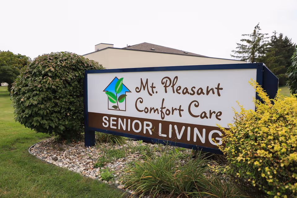 Outdoor sign reading "Mt. Pleasant Comfort Care Senior Living" on a landscaped lawn in front of the facility.