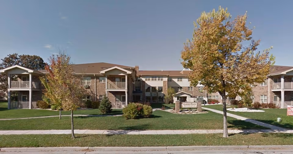 Exterior view of Garden Place Apartments with brick buildings, balconies, trees, and a central entrance sign.