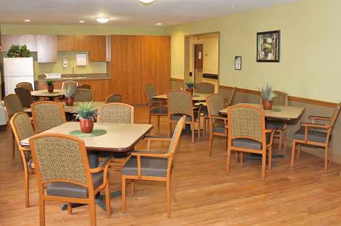 Senior living dining area with wooden tables, chairs, and potted plants.