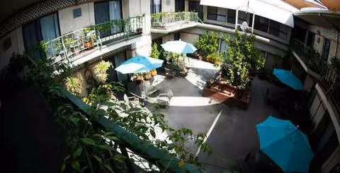 Courtyard with balconies, umbrellas, tables and chairs, greenery, and seating in a senior living facility.