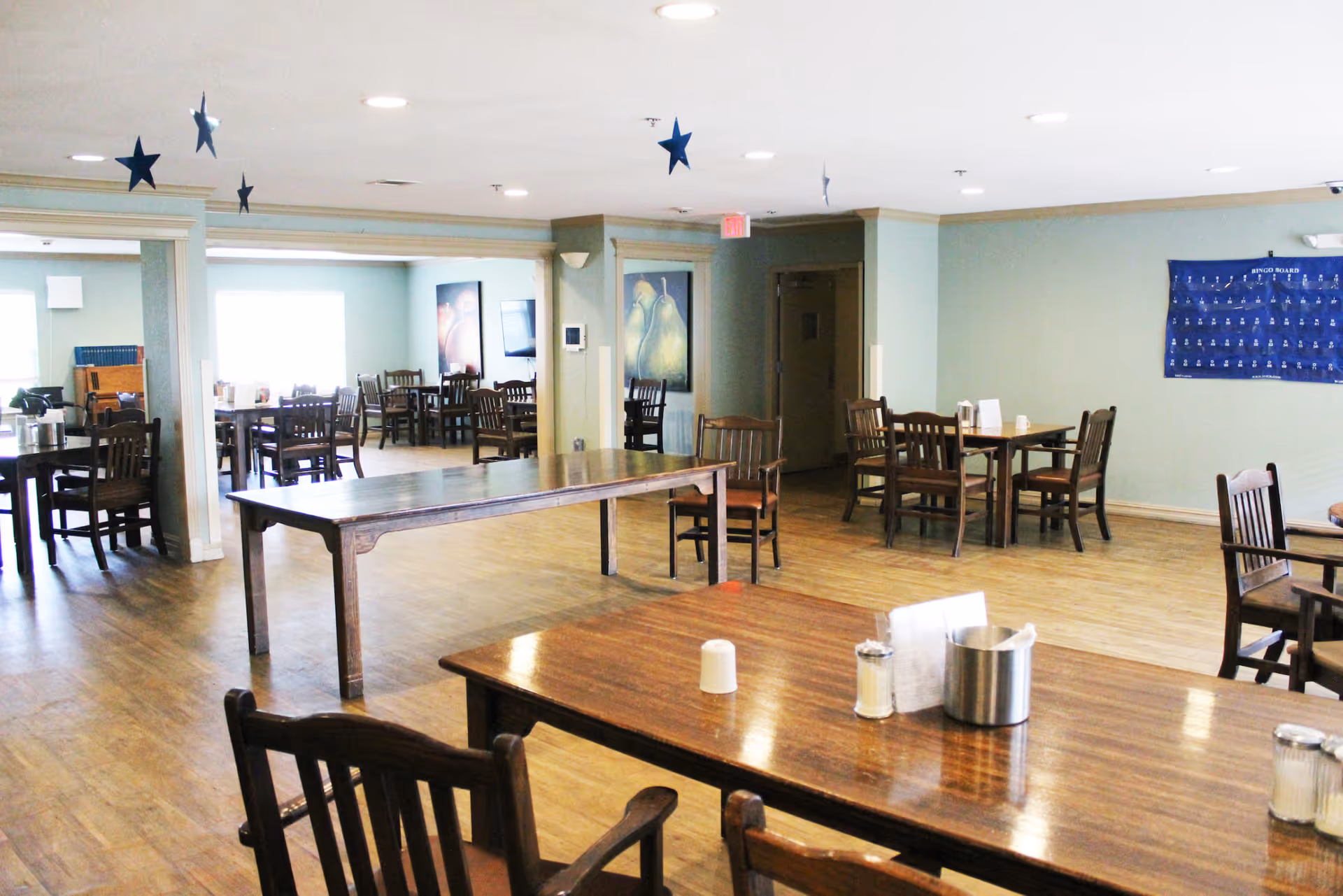 Spacious communal dining room with wooden tables and chairs and hardwood floors.