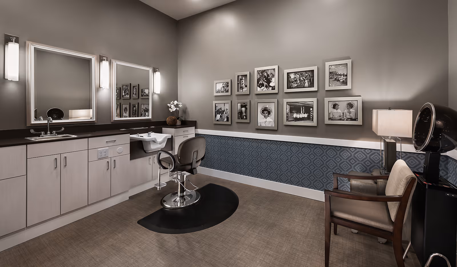 Salon-style interior with a styling chair, wash sink, mirrors, cabinetry and framed photos along the wall.