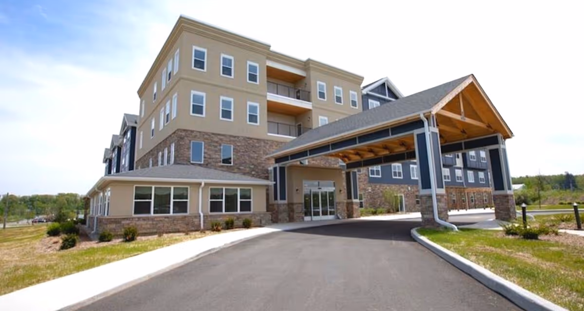 Front exterior of a multi-story senior living building with a covered porte-cochere entrance and driveway.