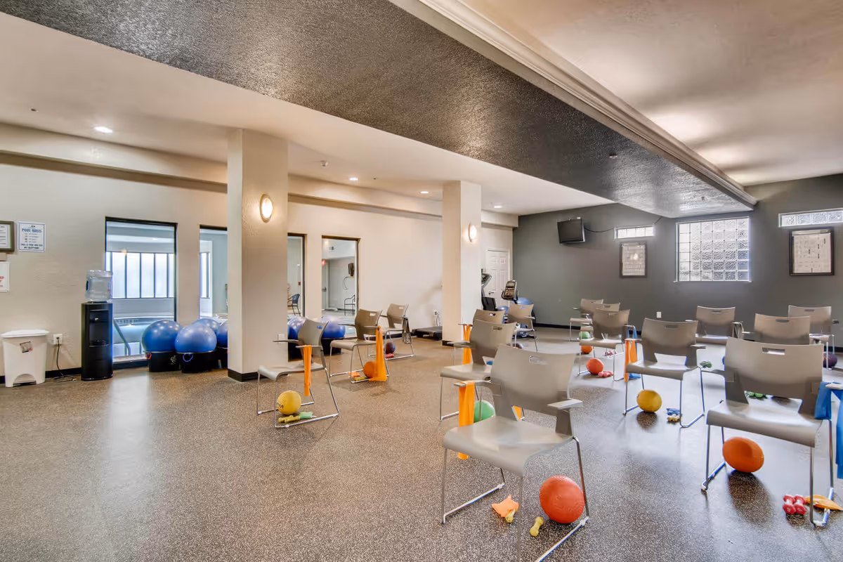 A spacious interior activity/exercise room with chairs, exercise balls, small weights and therapy equipment arranged across the floor.
