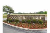 Stone entrance sign reading 'Wooldridge Place' set in a landscaped flowerbed with trees and a road nearby.