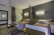 A shared senior living room with two single beds, matching nightstands, and a dark accent wall.