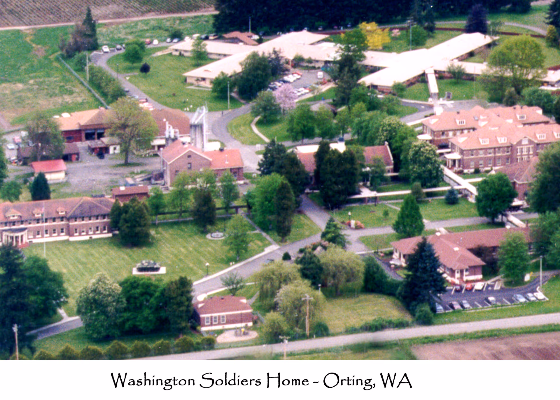Aerial view of the Washington State Soldiers Home in Orting, WA, showing multiple buildings surrounded by green lawns, trees, and pathways.