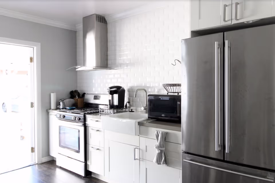 Bright modern kitchen with stainless steel refrigerator, stove, farmhouse sink, and white subway tile backsplash.