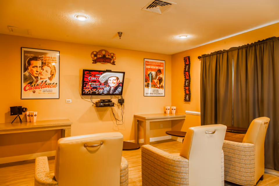 Cozy media room with armchairs facing a wall-mounted TV, movie posters, and side tables.