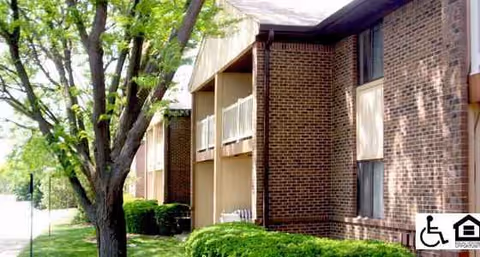 Brick exterior of a senior living apartment building with trees and shrubs.