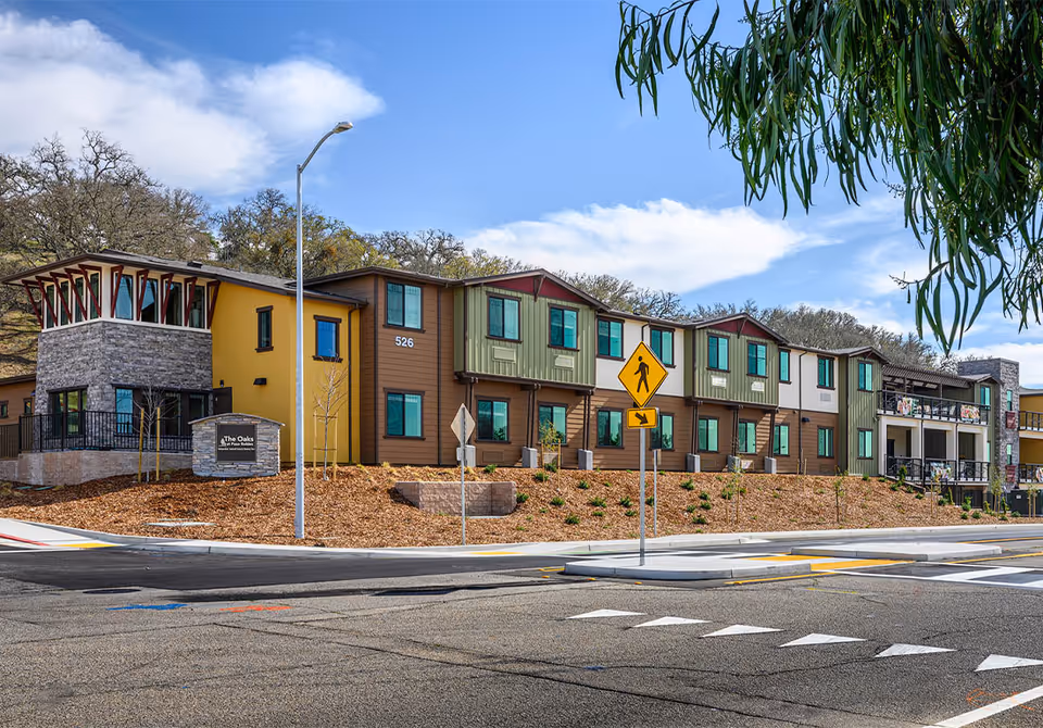 Street-front view of The Oaks at Paso Robles two-story senior living building with colorful siding, landscaping and a pedestrian crossing sign.