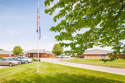 Facade of Majestic Care of Newburgh with flagpole, cars, and green lawn.