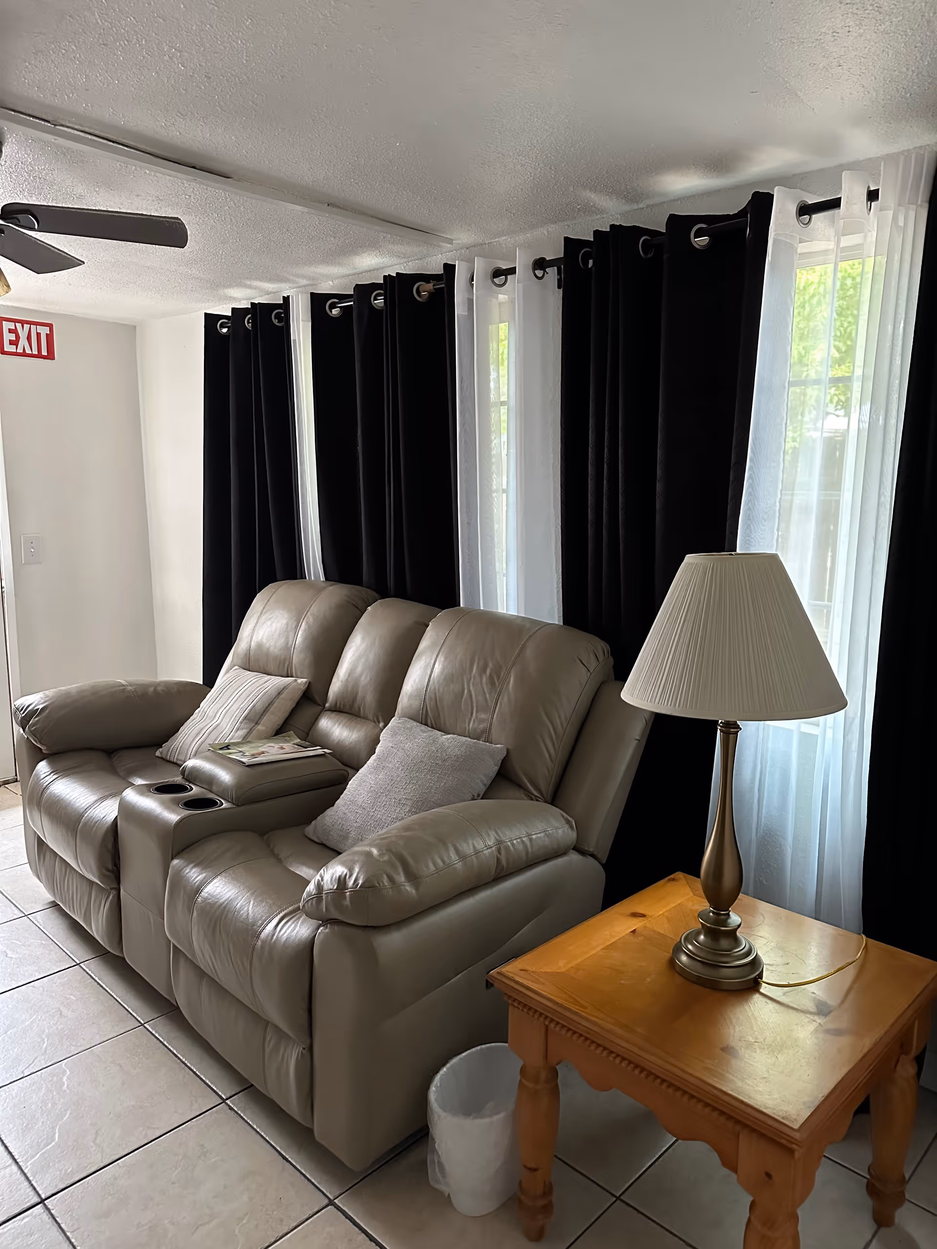 Leather reclining sofa with cushions, side table lamp, and dark-curtained windows in a living room.
