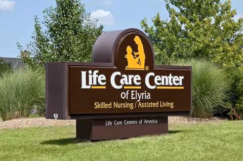 Outdoor sign for Life Care Center of Elyria on a grassy landscape.