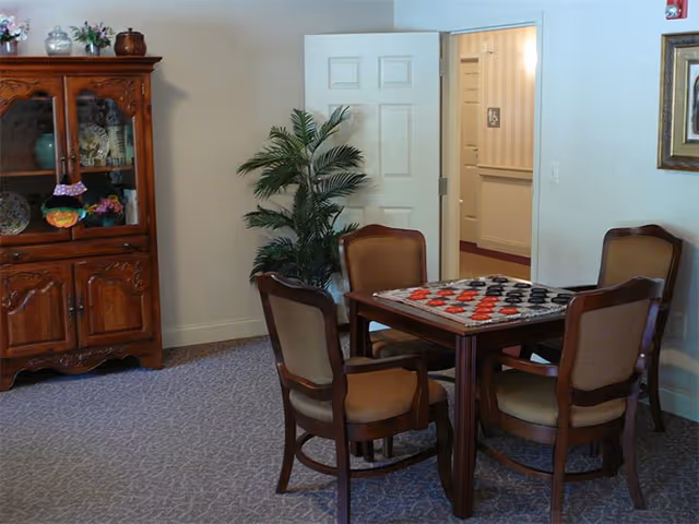 A small dining room in a senior facility with a wooden cabinet, plant, and checkered tabletop.